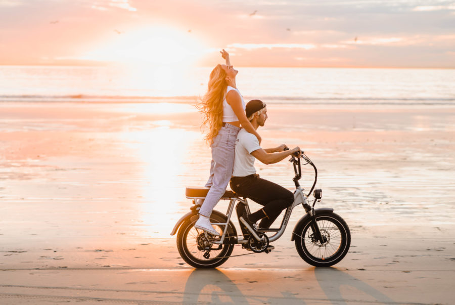 couple riding bike on the beach unique engagement photos