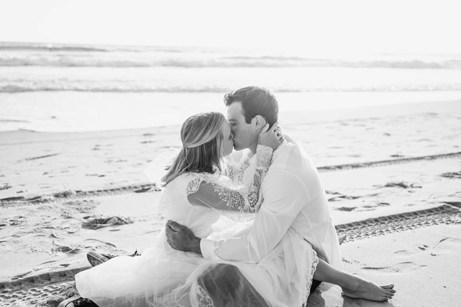 black and white couple kissing sitting on the beach