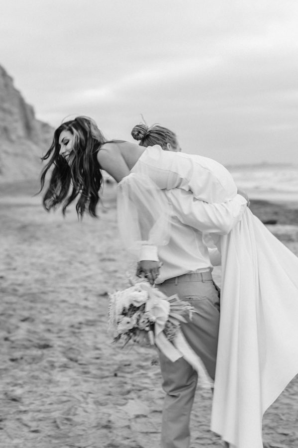black and white groom carry bride beach