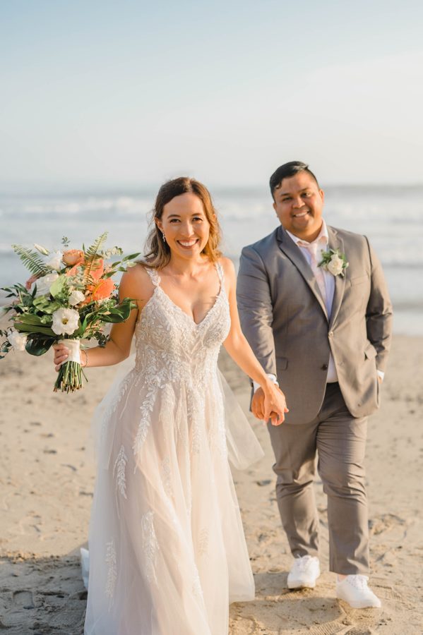 bride and groom smiling holding hands beach