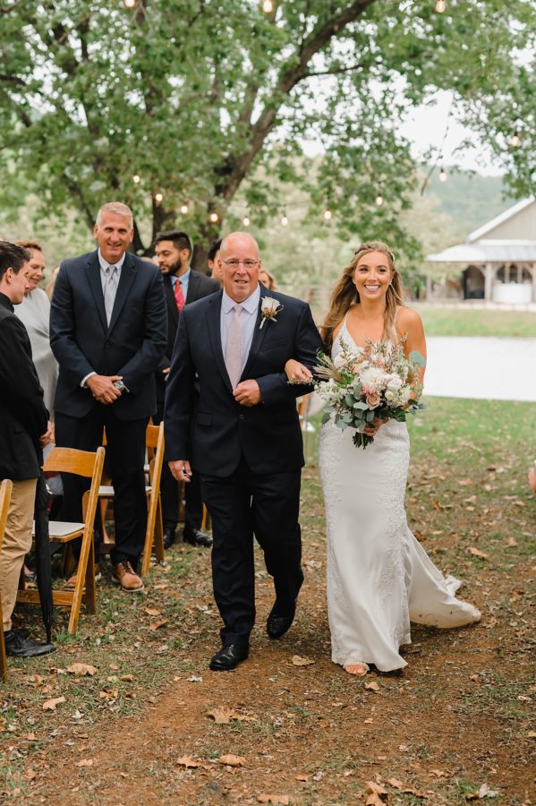 bride walking down aisle with father smiling