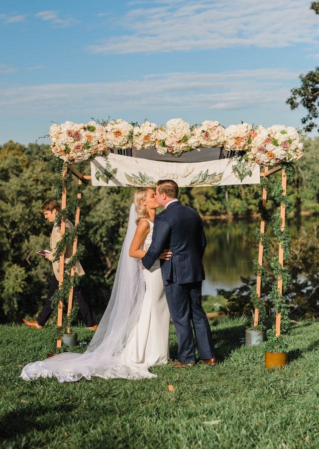 destination wedding bride and groom kissing floral arbor lakeside