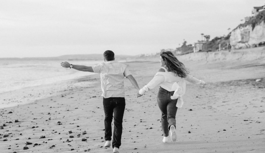 calafia beach engagement couple running holding hands black and white