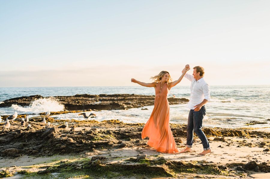 couple dancing on the rocks near the ocean while birds watch