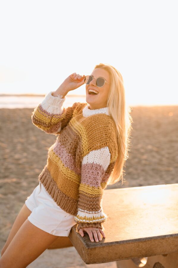 girl smiling during golden hour at the beach with sunglasses on 